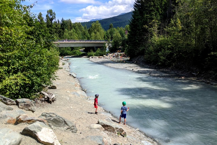 kids playing near the clear blue river that splits through Whistler village in the summer months